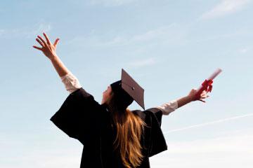 Chica con toga y birrete de graduación con los brazos abiertos celebrando